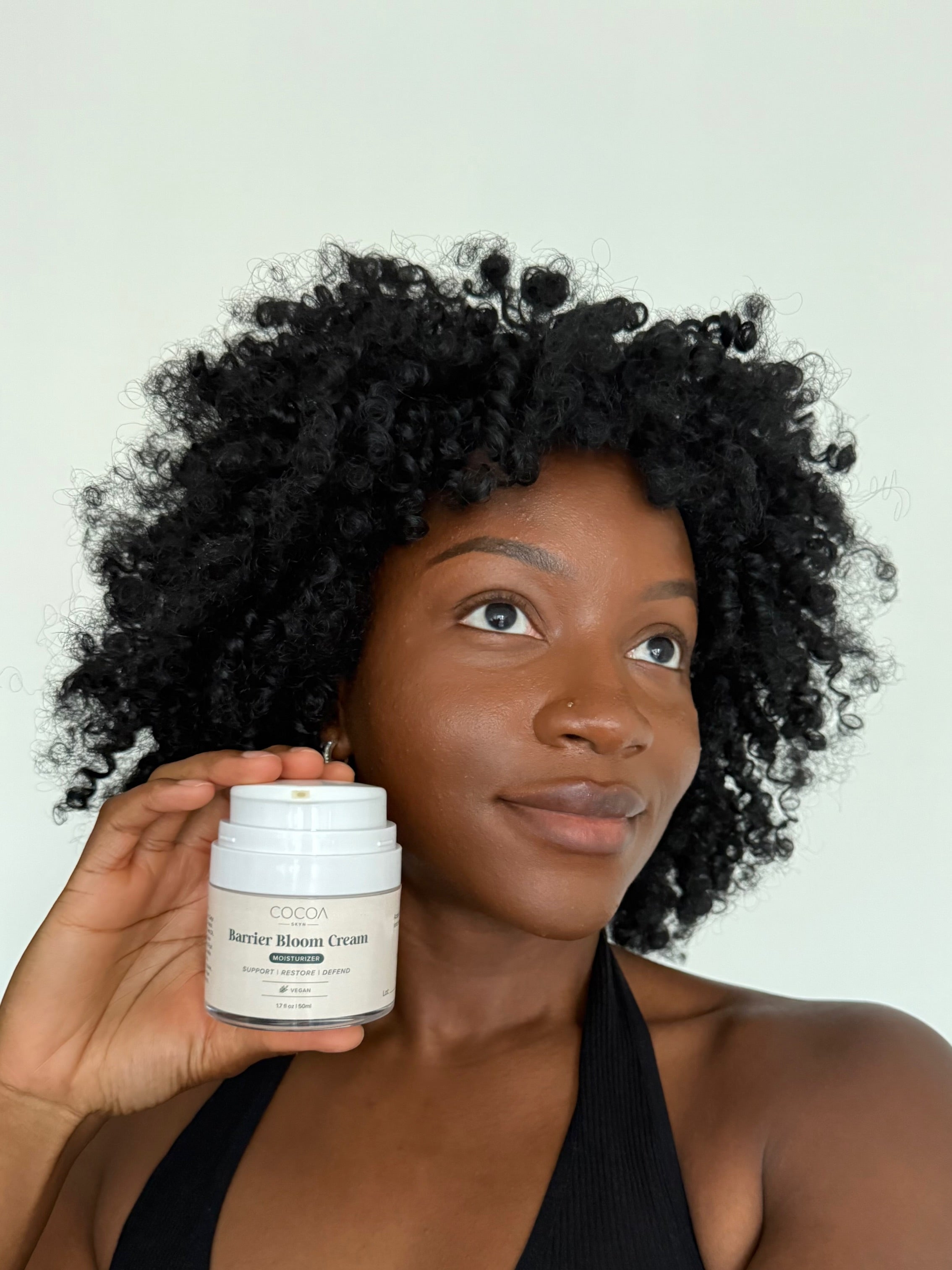 Woman holding a skincare product with a plain background